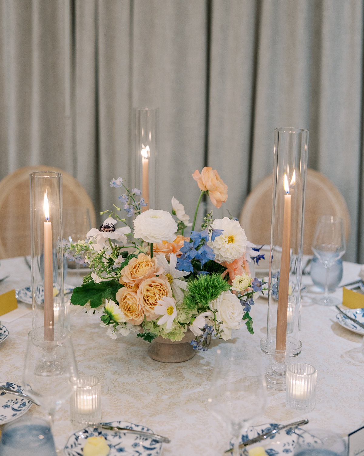 Romantic floral centerpiece in peach, ivory, and delphinium blue at Alila Marea wedding reception