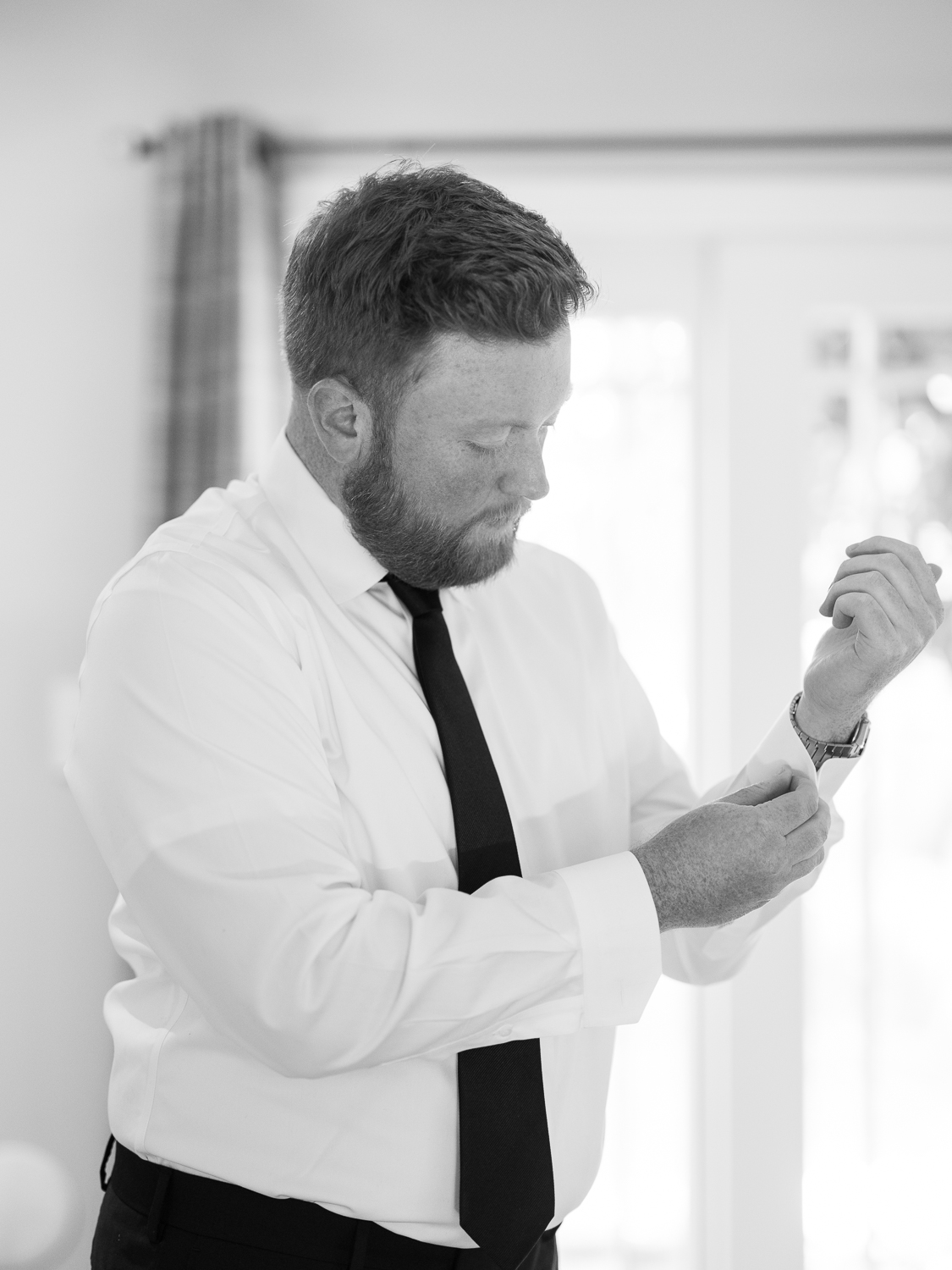 Black and white portrait of groom putting on Tiffany Co cufflinks