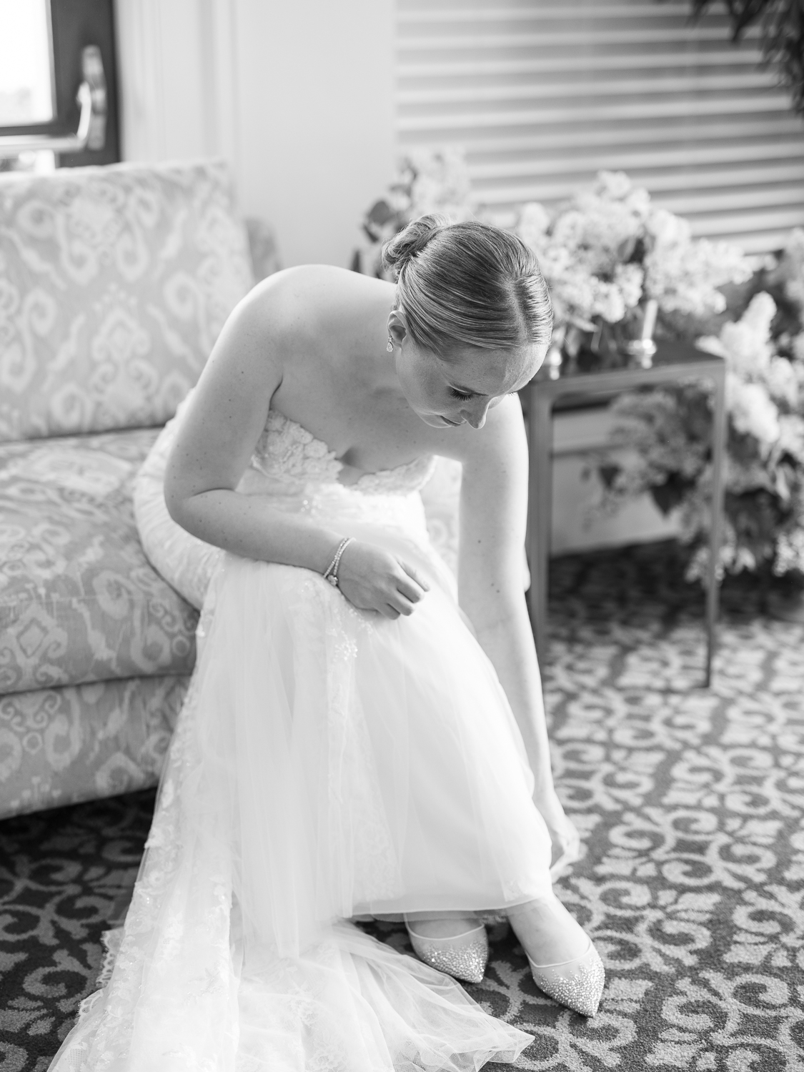 Black and white portrait of the bride putting on her Jimmy Choo bridal shoes