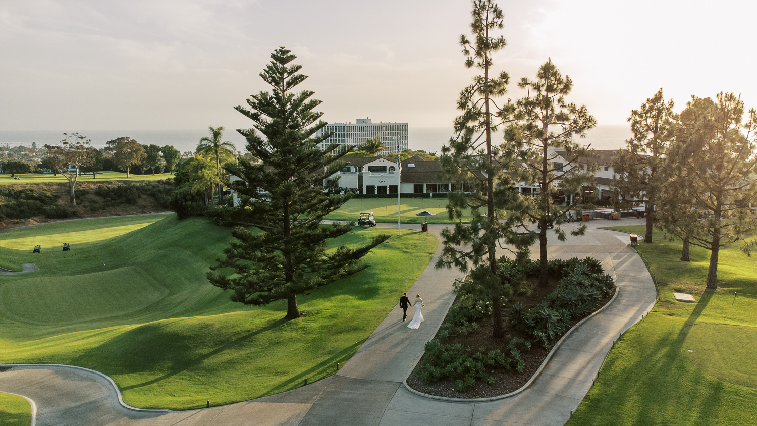 Drone photo of bride and groom walking to wedding cocktail hour during spring luxury La Jolla Country Club sunset